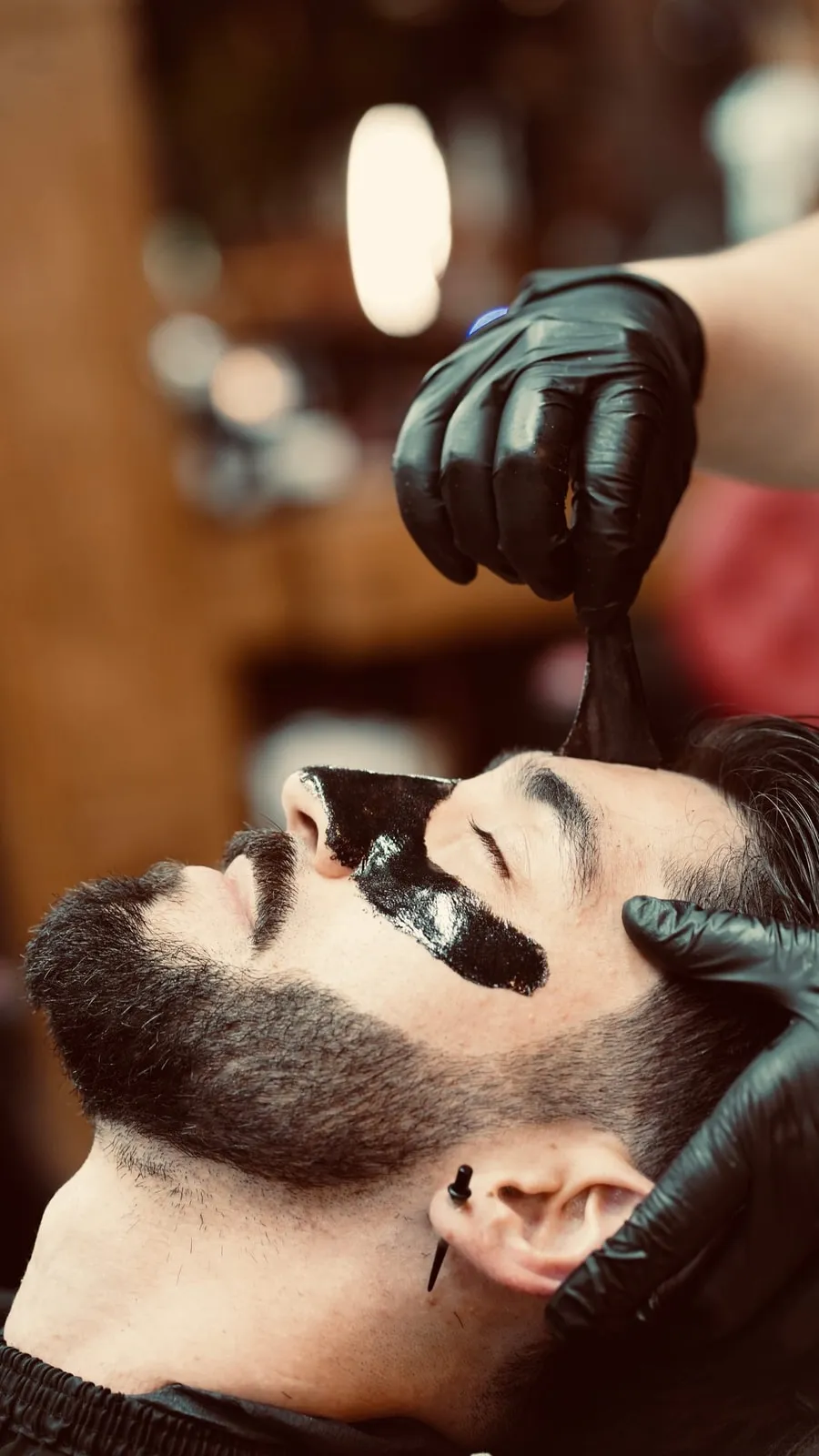 Barber peeling a black mask from a client's nose and under-eye area