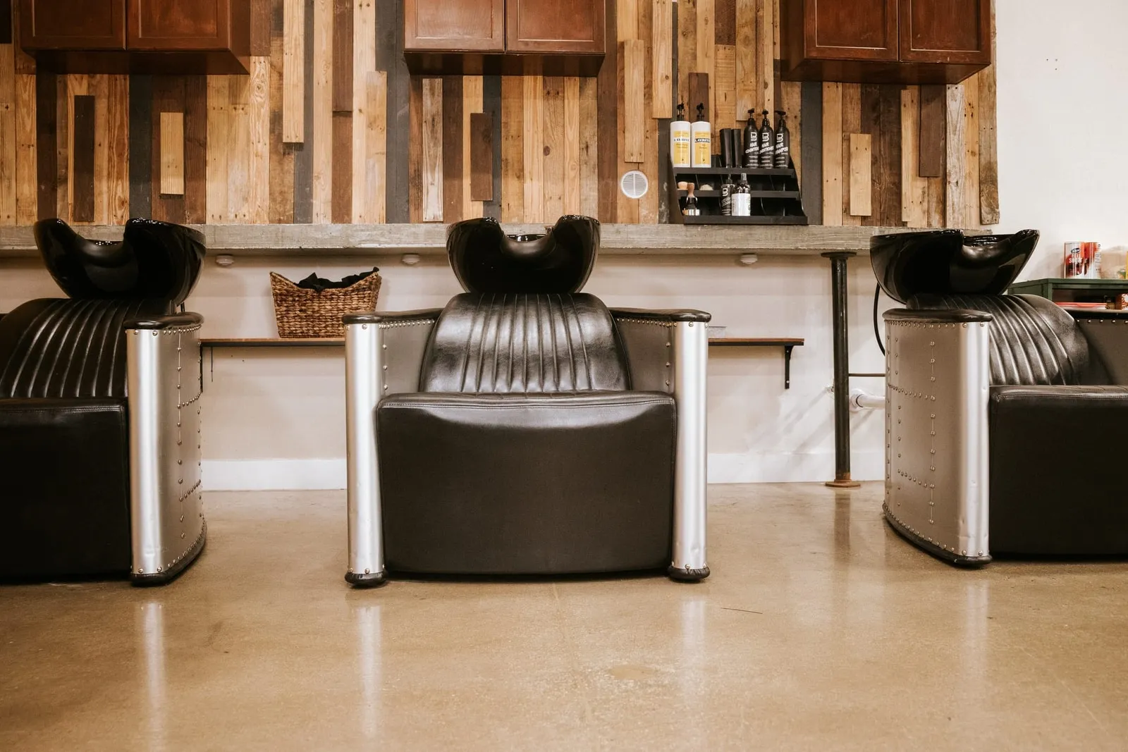 Three black shampoo chairs against a wood-plank wall