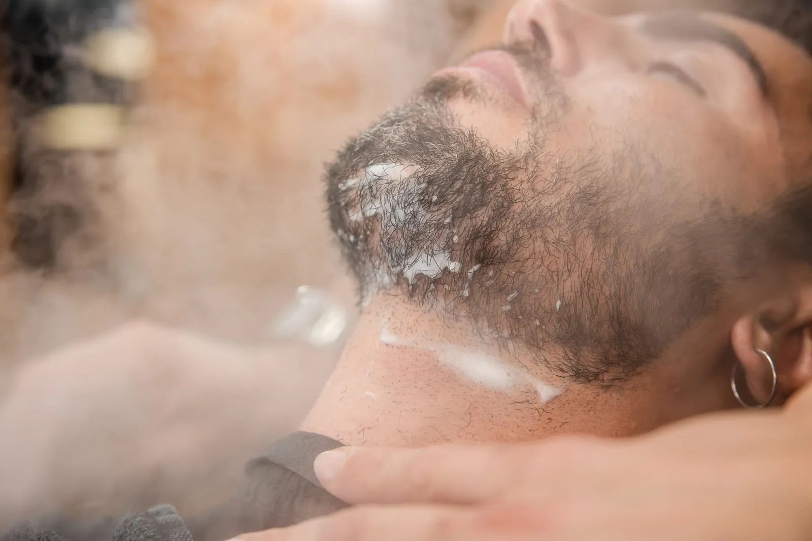Steam rising over shaving cream on a client's beard and neck