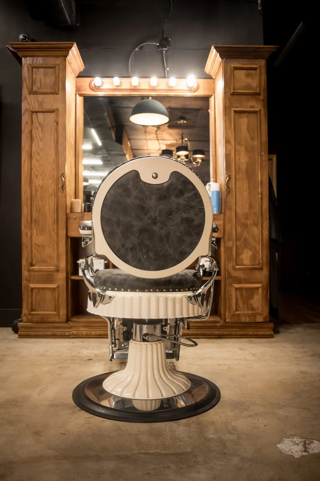 Vintage barber chair facing a wood station and lighted mirror
