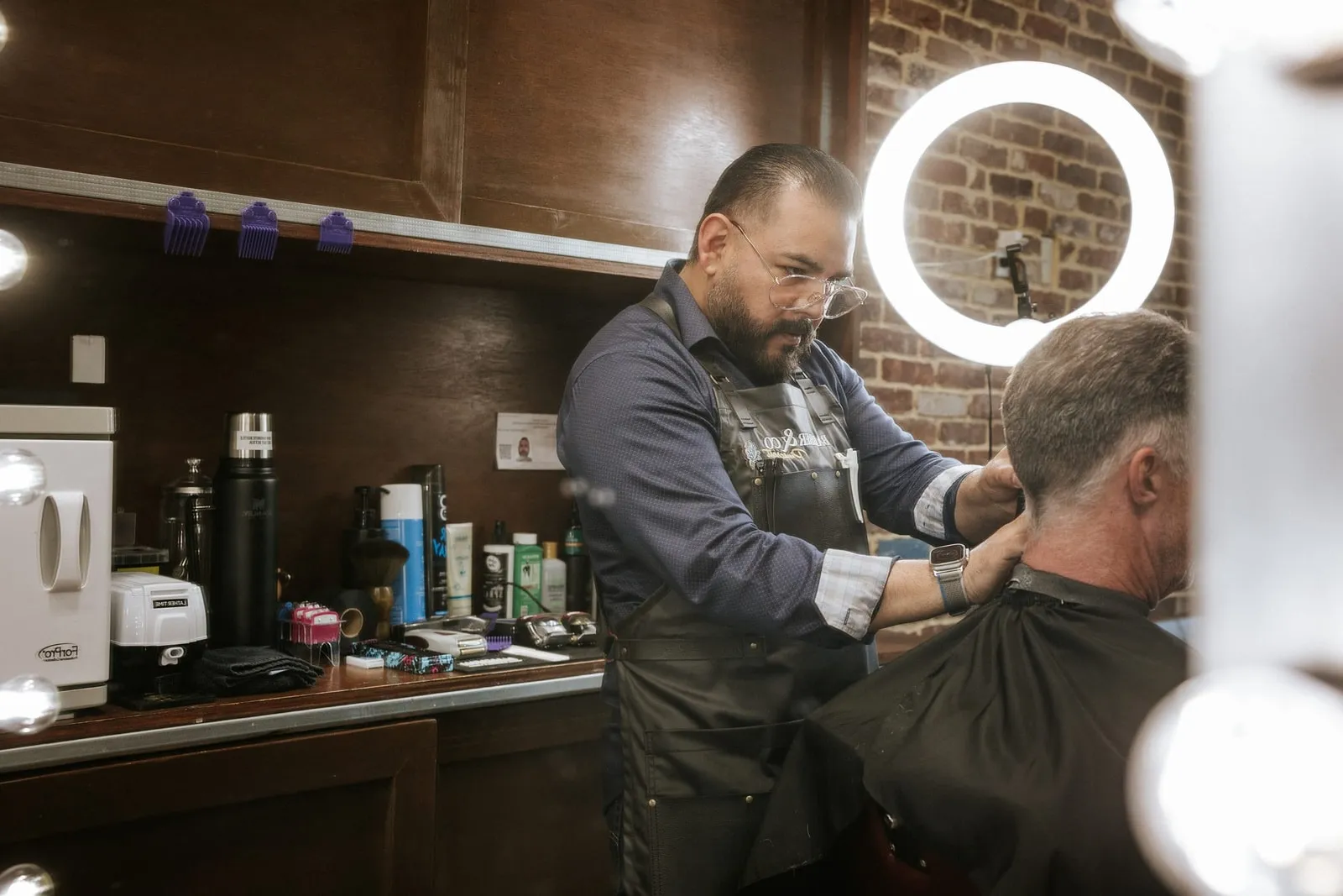 Barber trimming a client's neckline beside a ring light