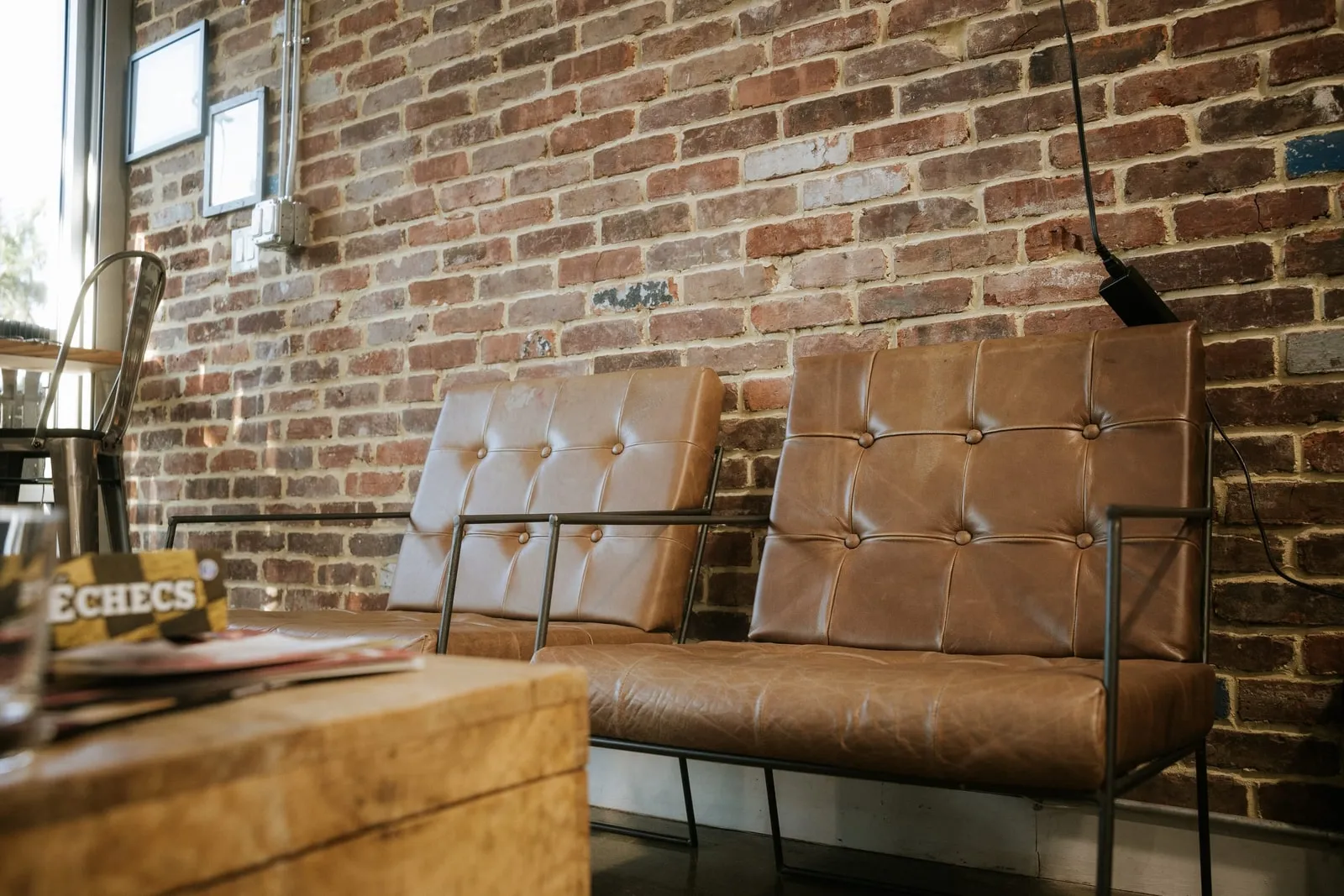 Two brown leather chairs against a brick waiting-area wall