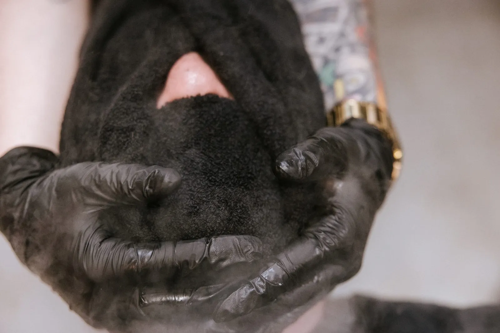 Gloved hands holding a steaming hot towel over a client's face